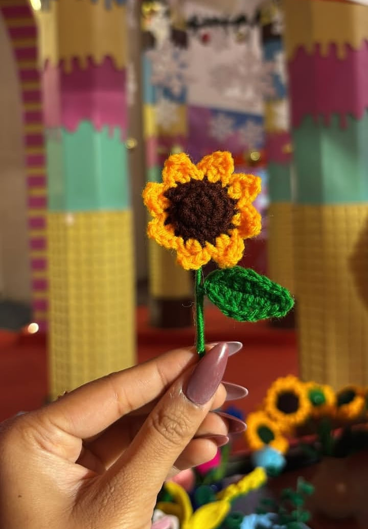 Hand holding a small sunflower decoration with colorful background