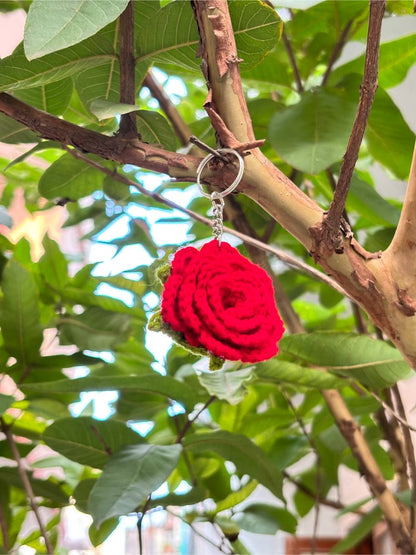 Red rose-shaped keychain hanging from a branch with green leaves in the background